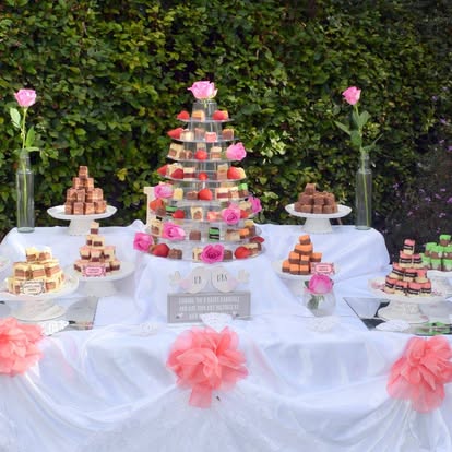 An outdoor dessert table decorated with pink flowers and fudge towers